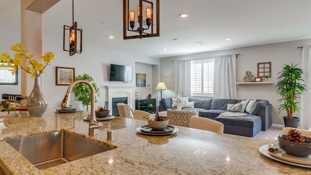 A modern kitchen with granite countertops, a stainless steel sink, and a dining area with a table and chairs. - 1000 MBPS Fast Wifi★Model Home★Luxury Family Retreat 5B/4b (Jurupa Valley)