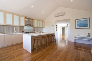 A modern kitchen with a central island, wooden bar stools, and a view of the living area.