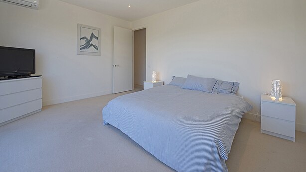 A modern bedroom with a large bed, bedside tables, a flat-screen TV, and a door leading to another room.
