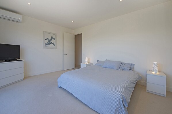A modern bedroom with a large bed, bedside tables, a flat-screen TV, and a door leading to another room.