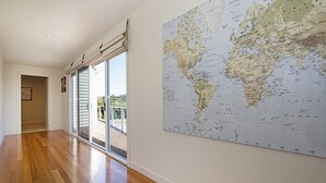 A spacious hallway with wooden flooring, a large world map on the wall, and a sliding glass door leading to an outdoor area.