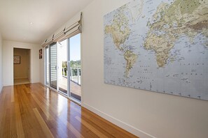 A spacious hallway with wooden flooring, a large world map on the wall, and a sliding glass door leading to an outdoor area.