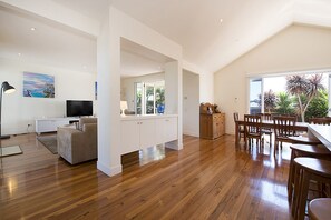 Un salón espacioso con piso de madera, un sofá, un televisor y un comedor con sillas y mesa de madera.