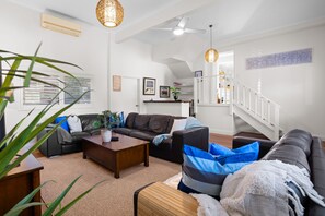 A modern living room with a brown leather sofa, a wooden coffee table, and a staircase leading to an upper level. - Sea Ranch Rye Coastal Retreat Pool Tennis court (RYE)
