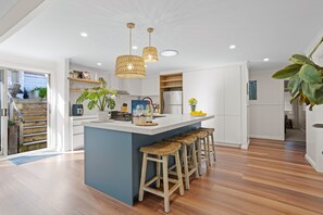 A modern kitchen with a central island, bar stools, and a view of the outdoor area.