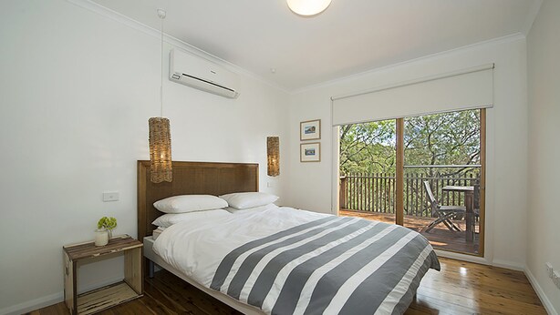 Una camera da letto con un letto, un comodino, un condizionatore d'aria a muro e vista su una terrazza.