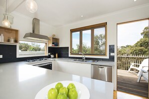 A modern kitchen with a large island, stainless steel appliances, and a view of the outdoors. - Treetops Coastal Family Retreat in Sorrento (SORRENTO)