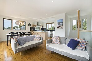 A modern living space with a dining area, kitchen, and large windows. - Treetops Coastal Family Retreat in Sorrento (SORRENTO)