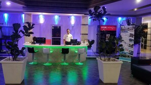 A reception area with a counter, a man standing behind it, and potted plants.