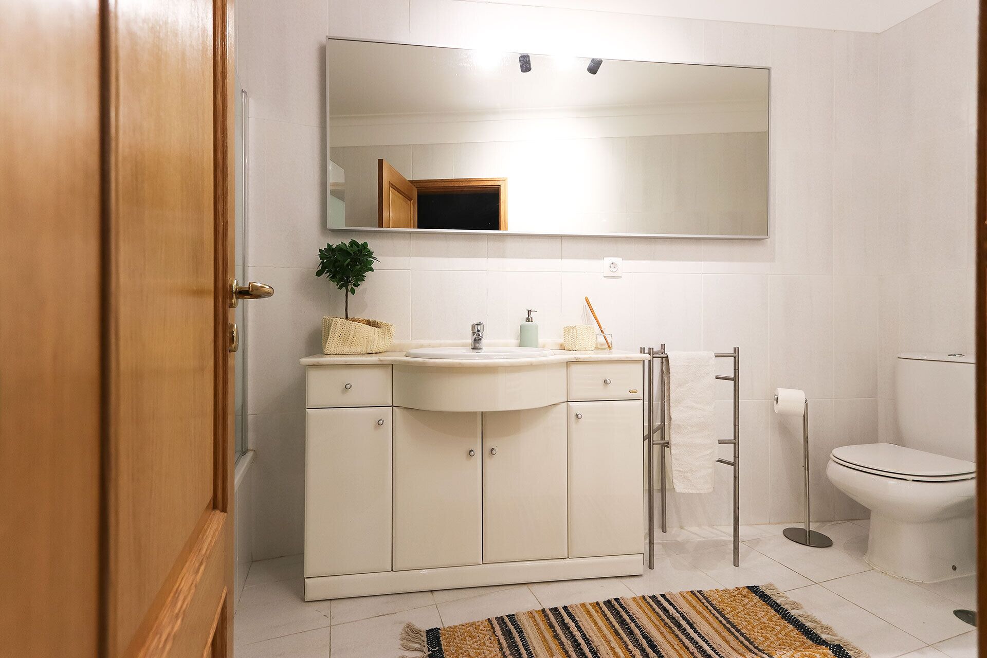 A bathroom with a white vanity, a mirror, a small plant, a towel rack, and a toilet.