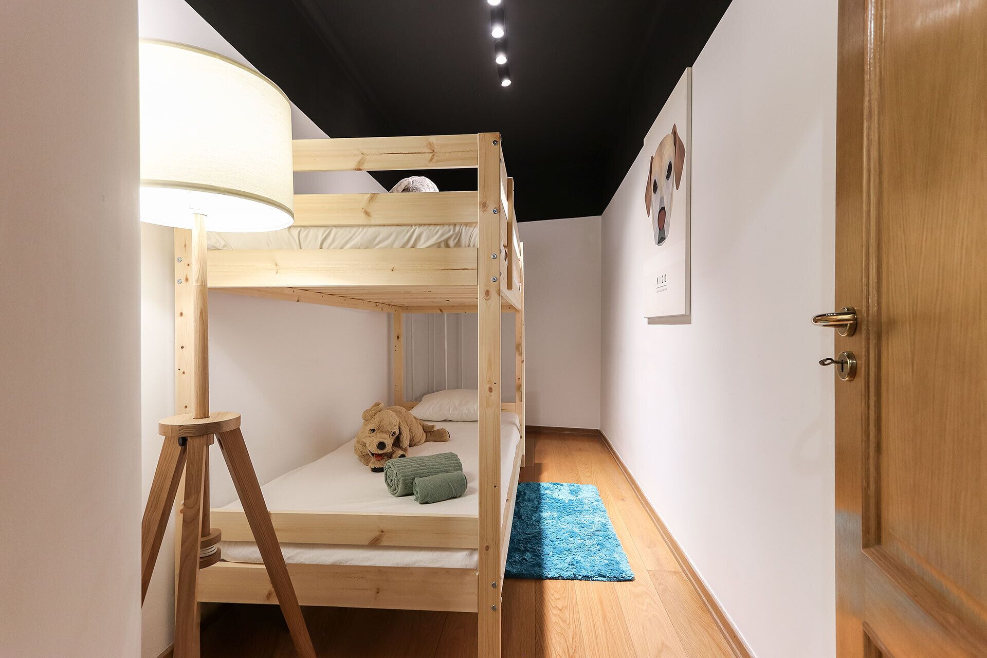 Une chambre avec un lit superposé, une échelle en bois, une petite table et un ours en peluche.
