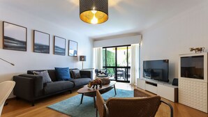 A modern living room with a sofa, coffee table, and wicker chair. A television and cabinet are visible. - Luxurious & Modern central apt w / 4 rooms, private terrace and 2 parking spaces (Lisboa)