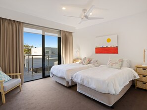 A hotel room with two beds, a ceiling fan, a large window with curtains, a wall-mounted artwork, and a view of the outside.