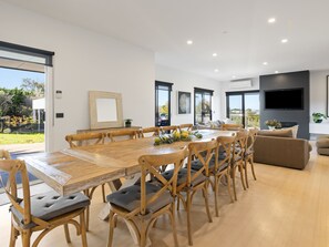 A modern dining area with a large wooden table and chairs, a flat-screen TV, and a view of the outdoors. - Corfu Sorrento with magnesium pool (SORRENTO)