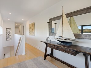 A modern interior with a wooden console table, a sailboat model, and a large mirror reflecting a window view.