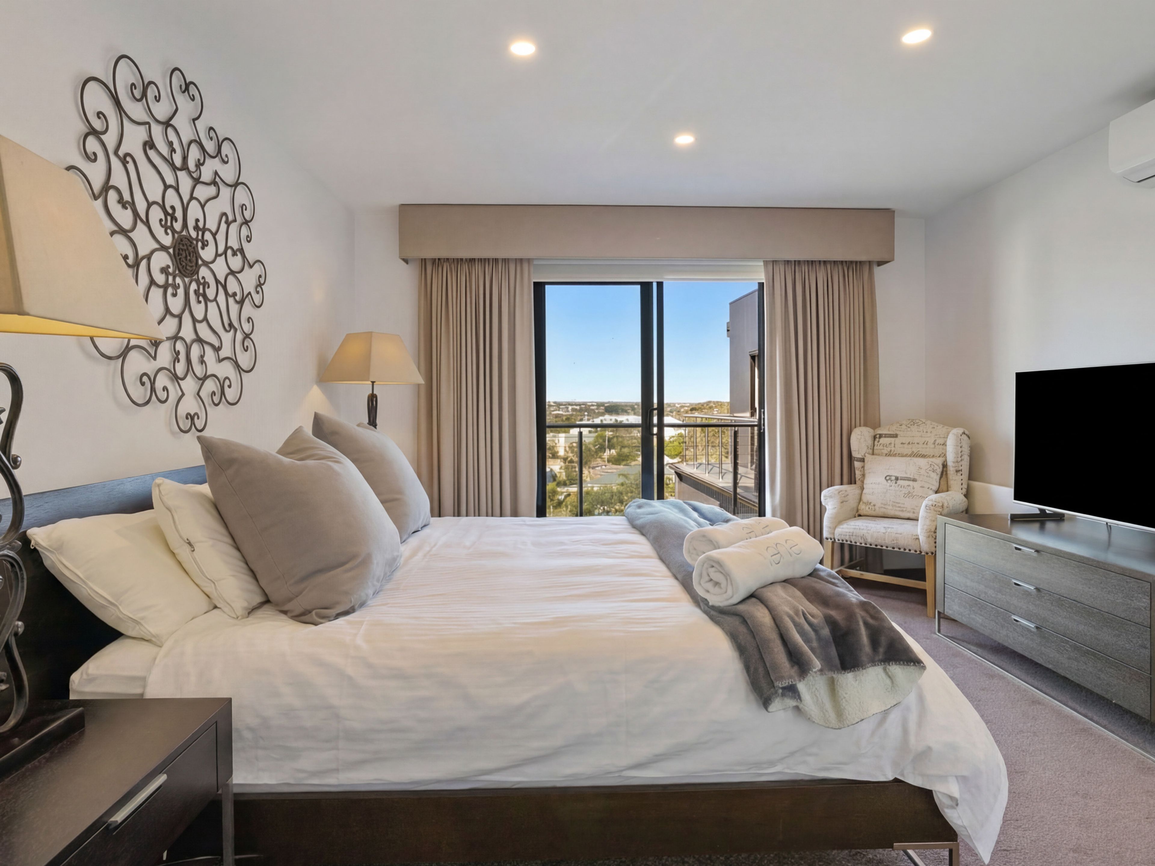 A hotel room with a large bed, a TV, a chair, and a view of the city.