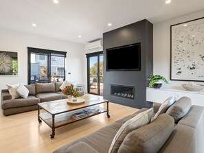 A modern living room with a sofa, coffee table, fireplace, and a TV mounted on the wall.