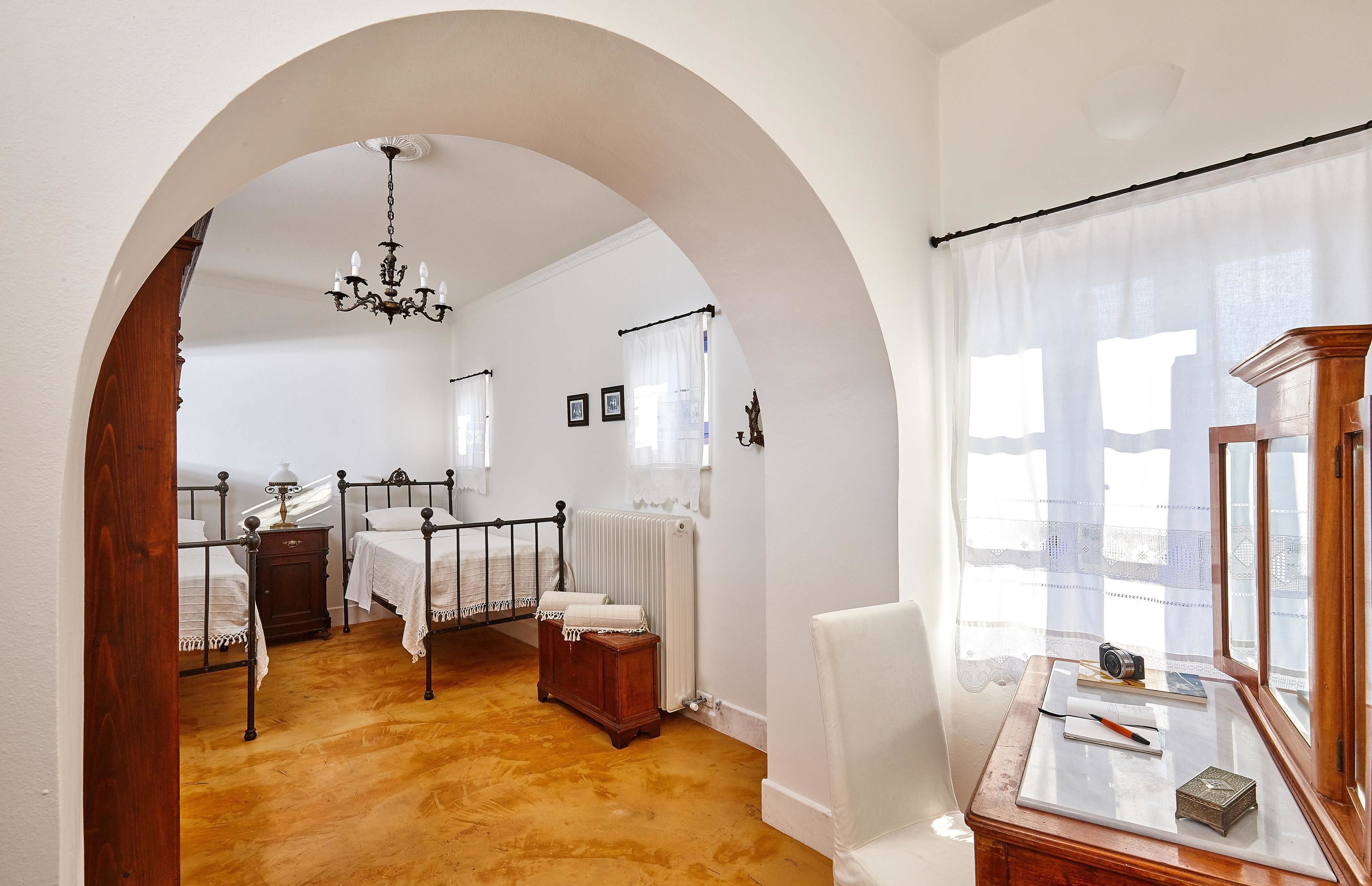 Un dormitorio con dos camas, un aparador de madera, un escritorio con silla y un amplio arco de entrada.