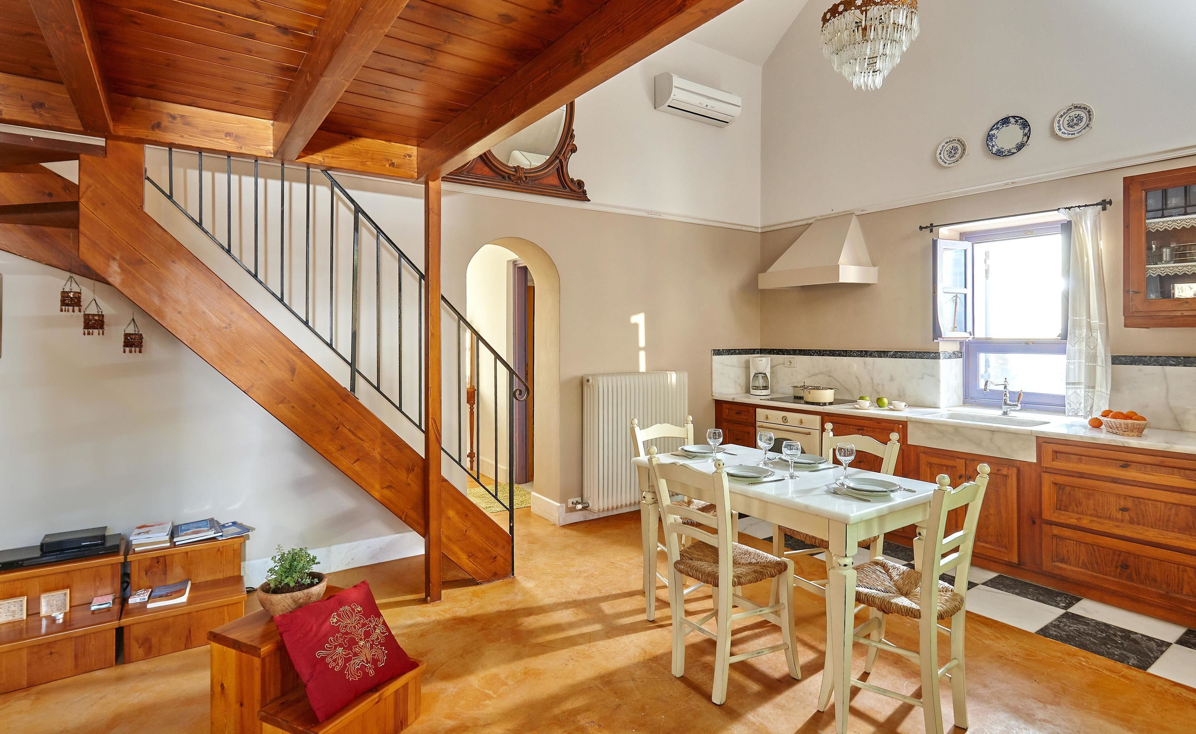A spacious kitchen with a dining area, wooden staircase, and a view of the outdoors.