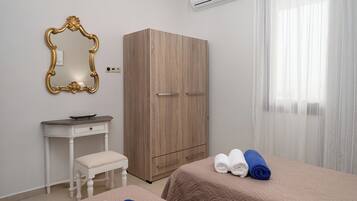 A hotel room with a wooden wardrobe, a small white desk with a chair, a bed with two rolled towels, and a large mirror with an ornate frame.