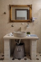 Un baño con un lavabo redondo, un espejo con marco dorado, una toalla y un secador de pelo en la pared.
