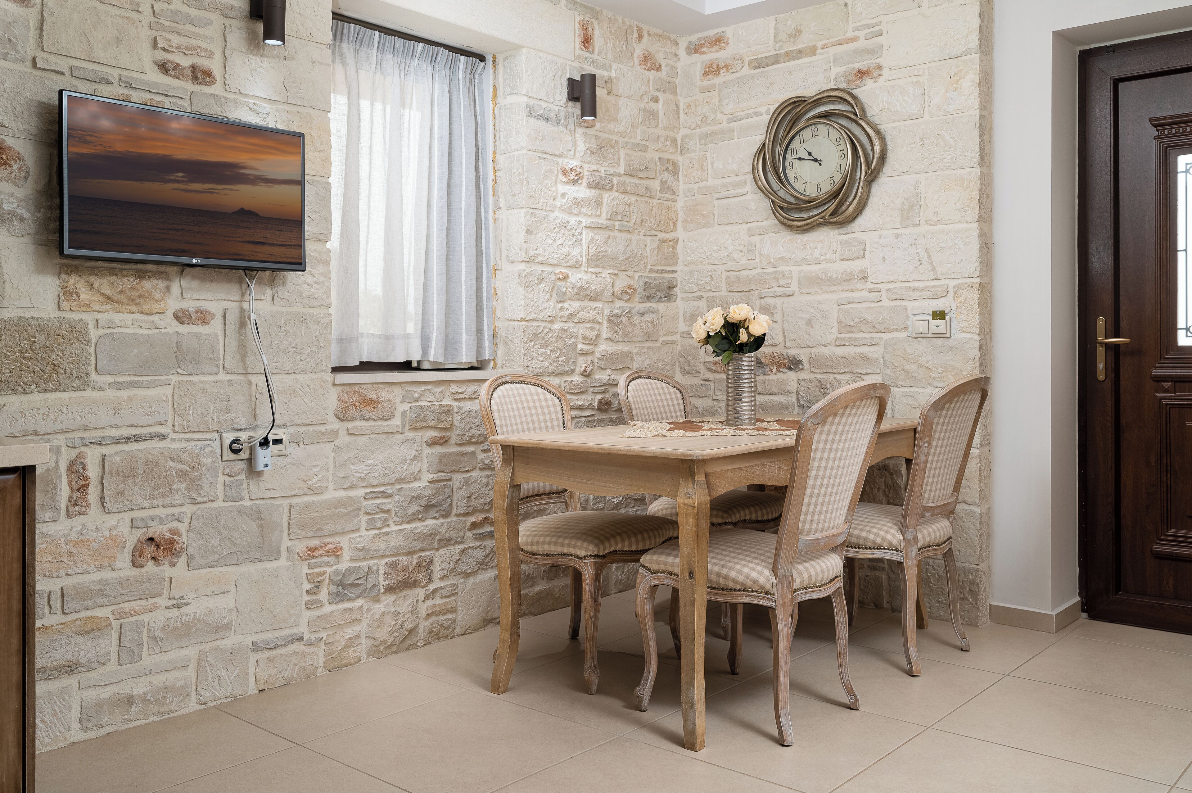 A dining area with a stone wall, a wooden table, and wicker chairs.