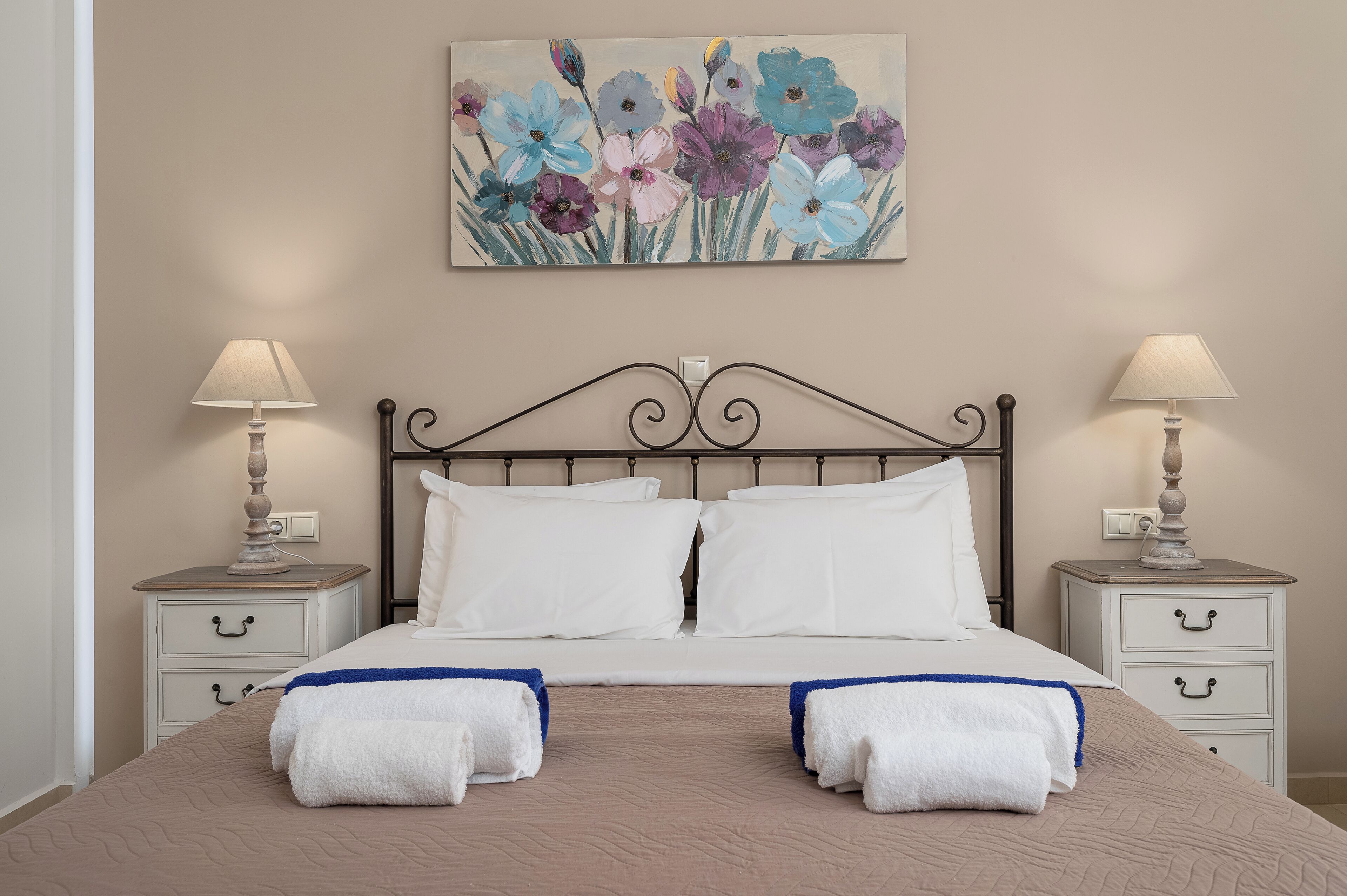 A neatly made bed with white linens and blue accents, flanked by two bedside tables with lamps and drawers.