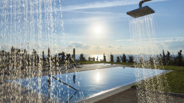 Ein Pool mit Brause, umgeben von einer gepflasterten Fläche und Blick auf das Meer.