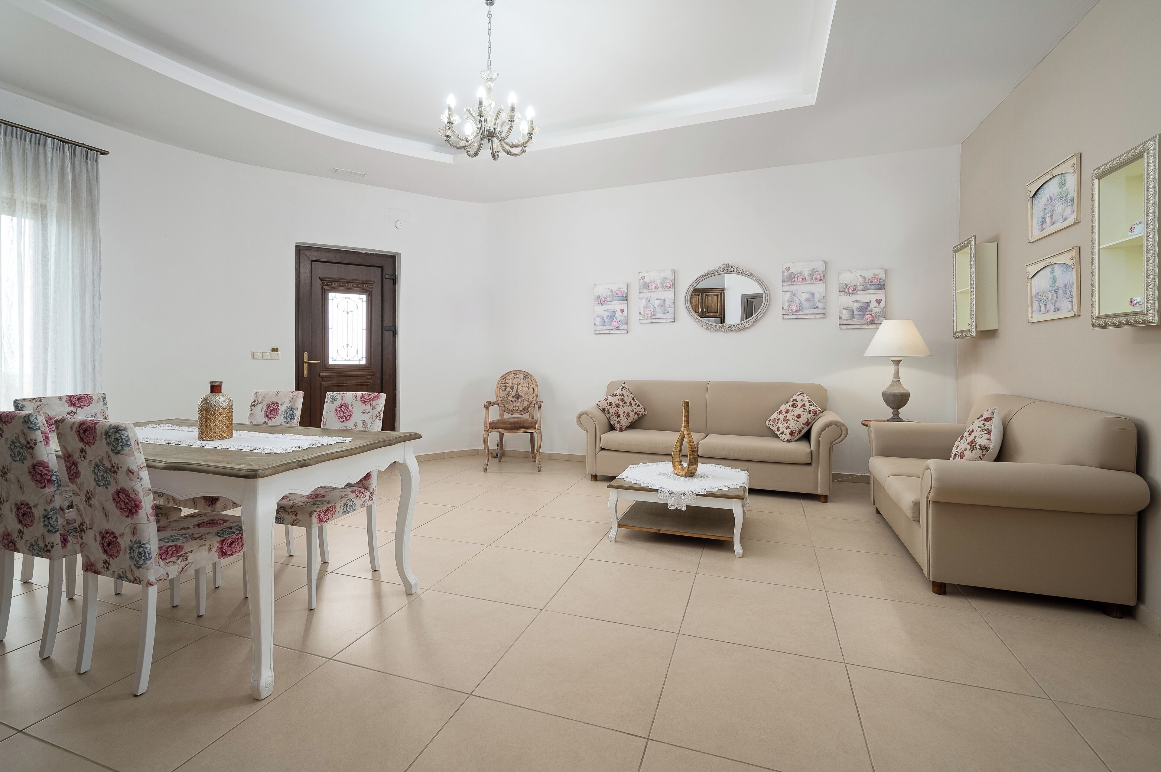 A living room with a dining table, floral chairs, a sofa, a coffee table, and a chandelier.