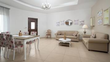 A living room with a dining table, floral chairs, a sofa, a coffee table, and a chandelier.