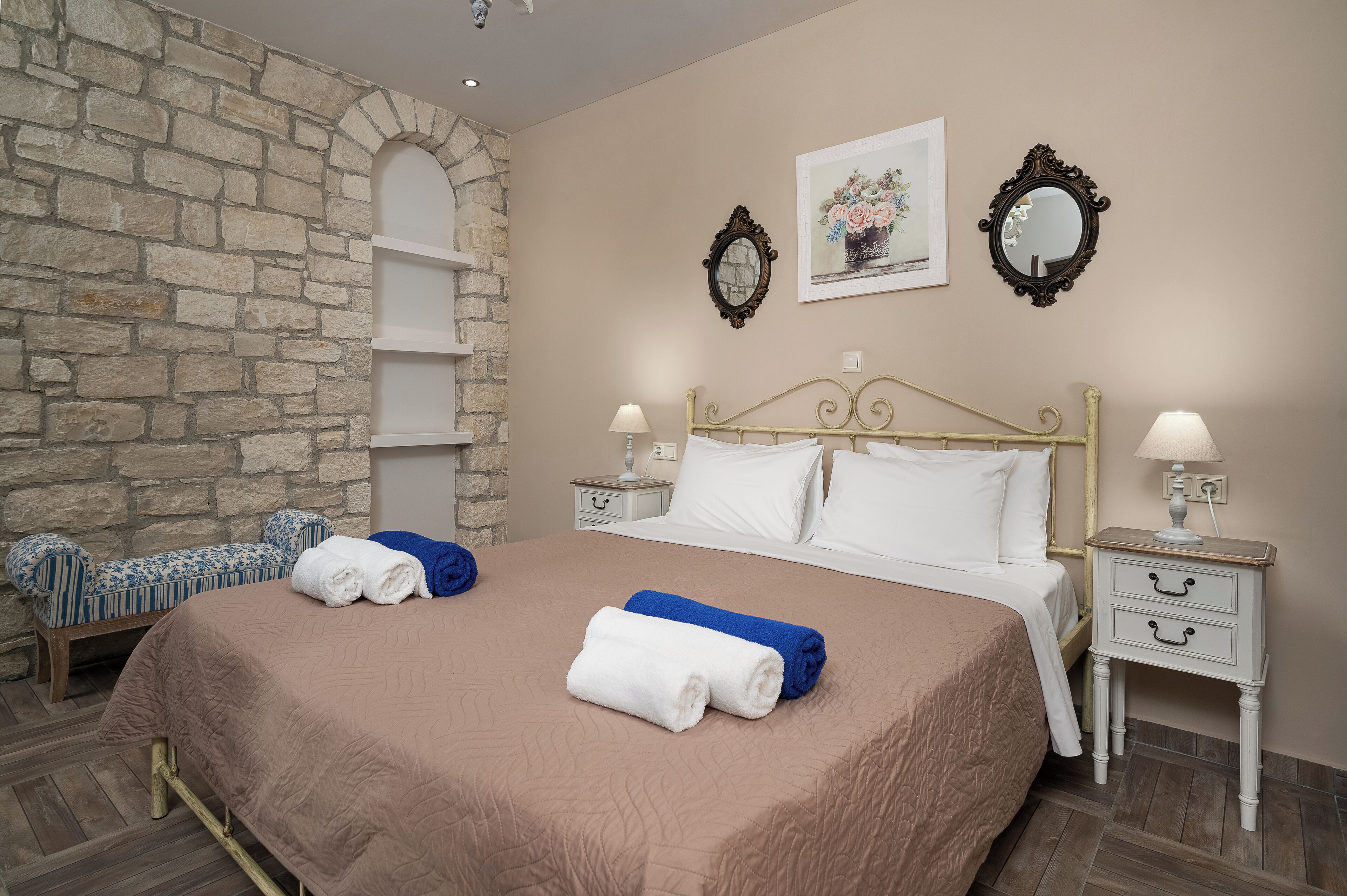 A neatly made bed with white and blue towels, a stone wall, and a wooden bench.