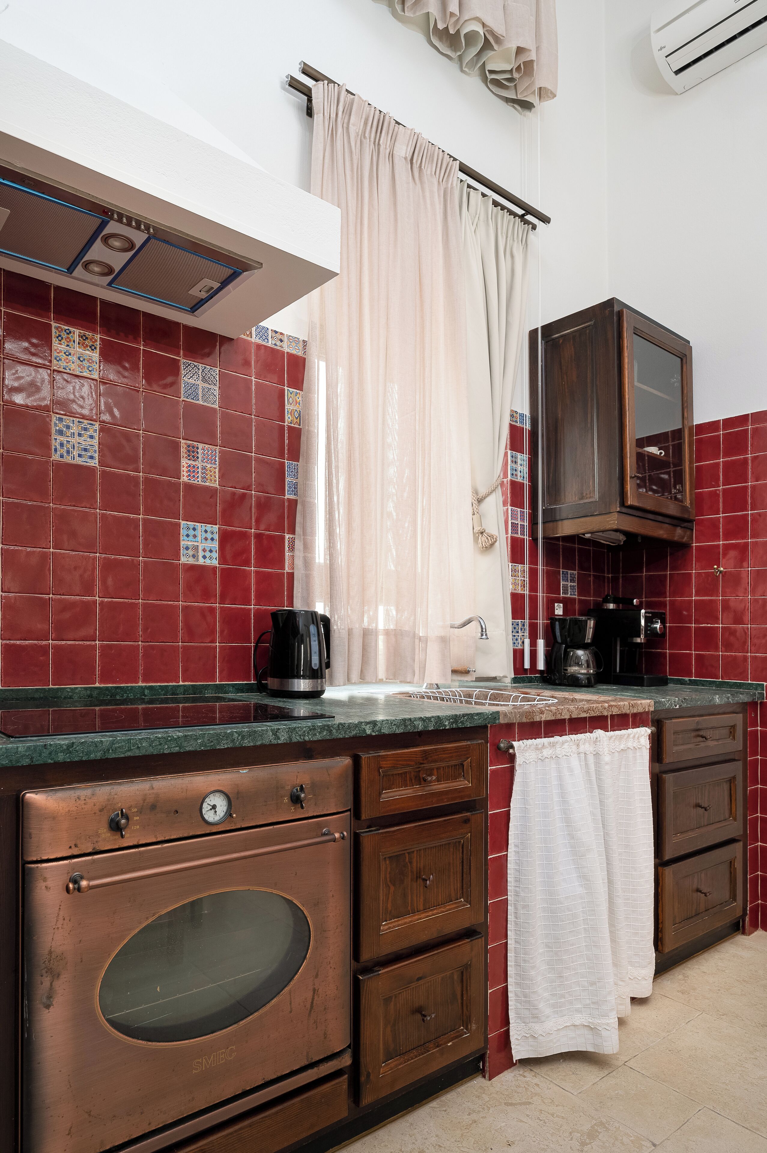 Una cocina con baldosas rojas, un hervidor de acero inoxidable, una cafetera y un horno de madera.