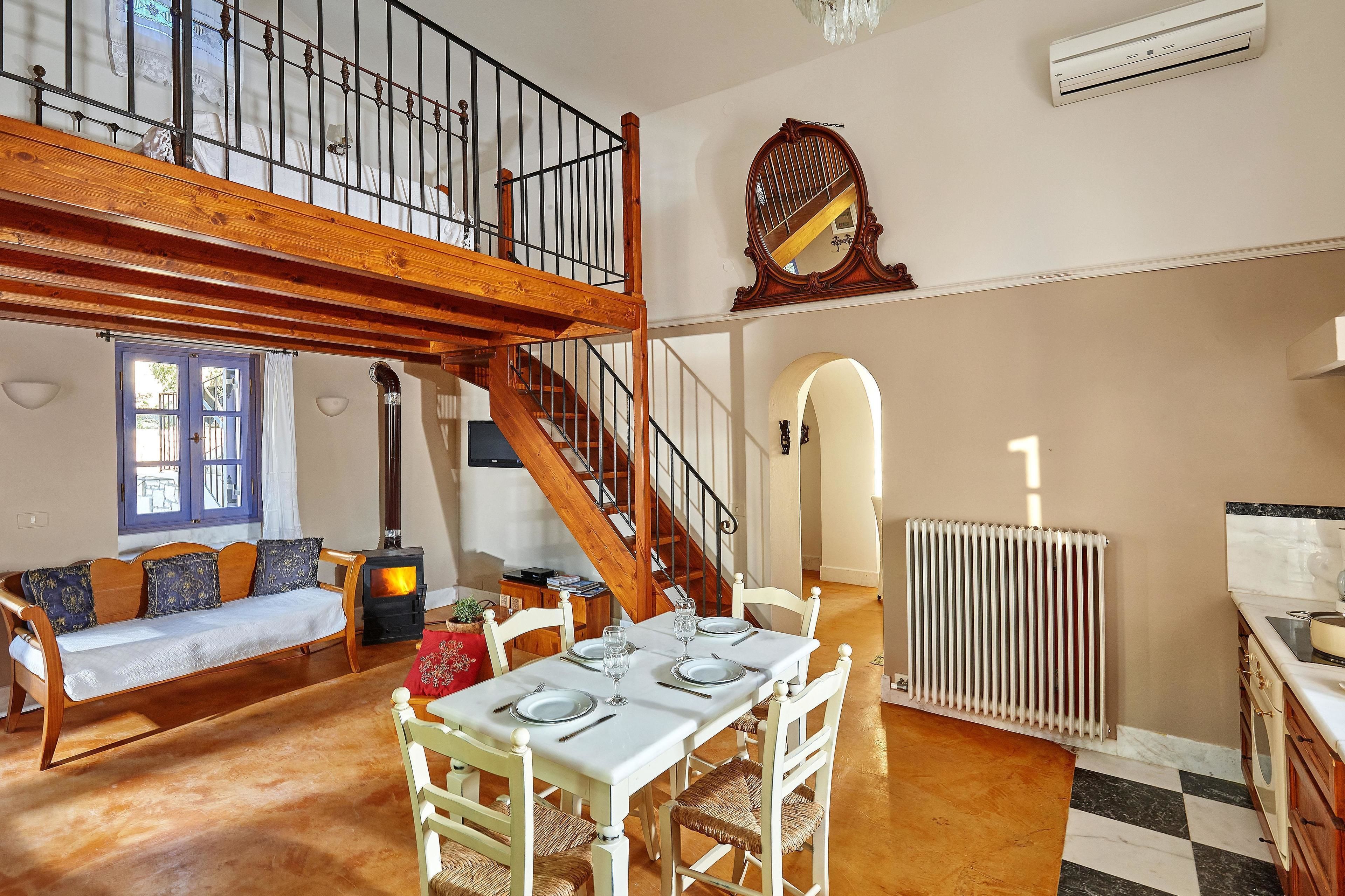 A spacious living area with a wooden staircase, a dining table set for four, a sofa, and a radiator.