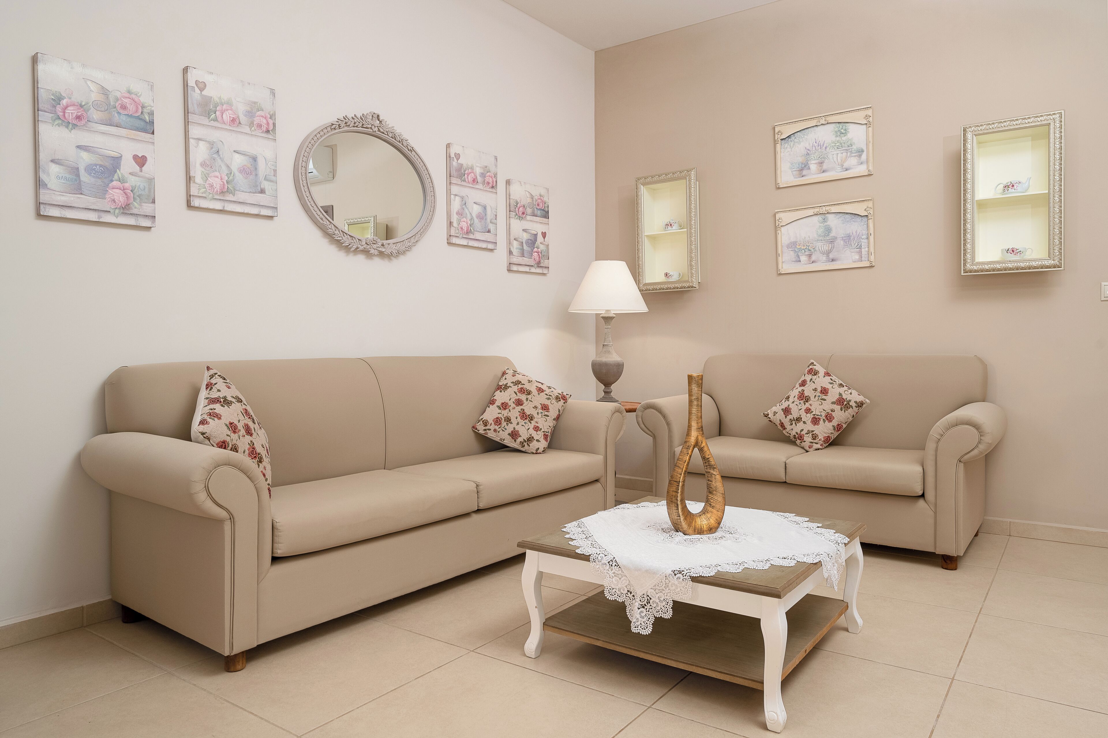 A living room with two beige sofas, a coffee table, a mirror, and wall-mounted shelves with decorative items.