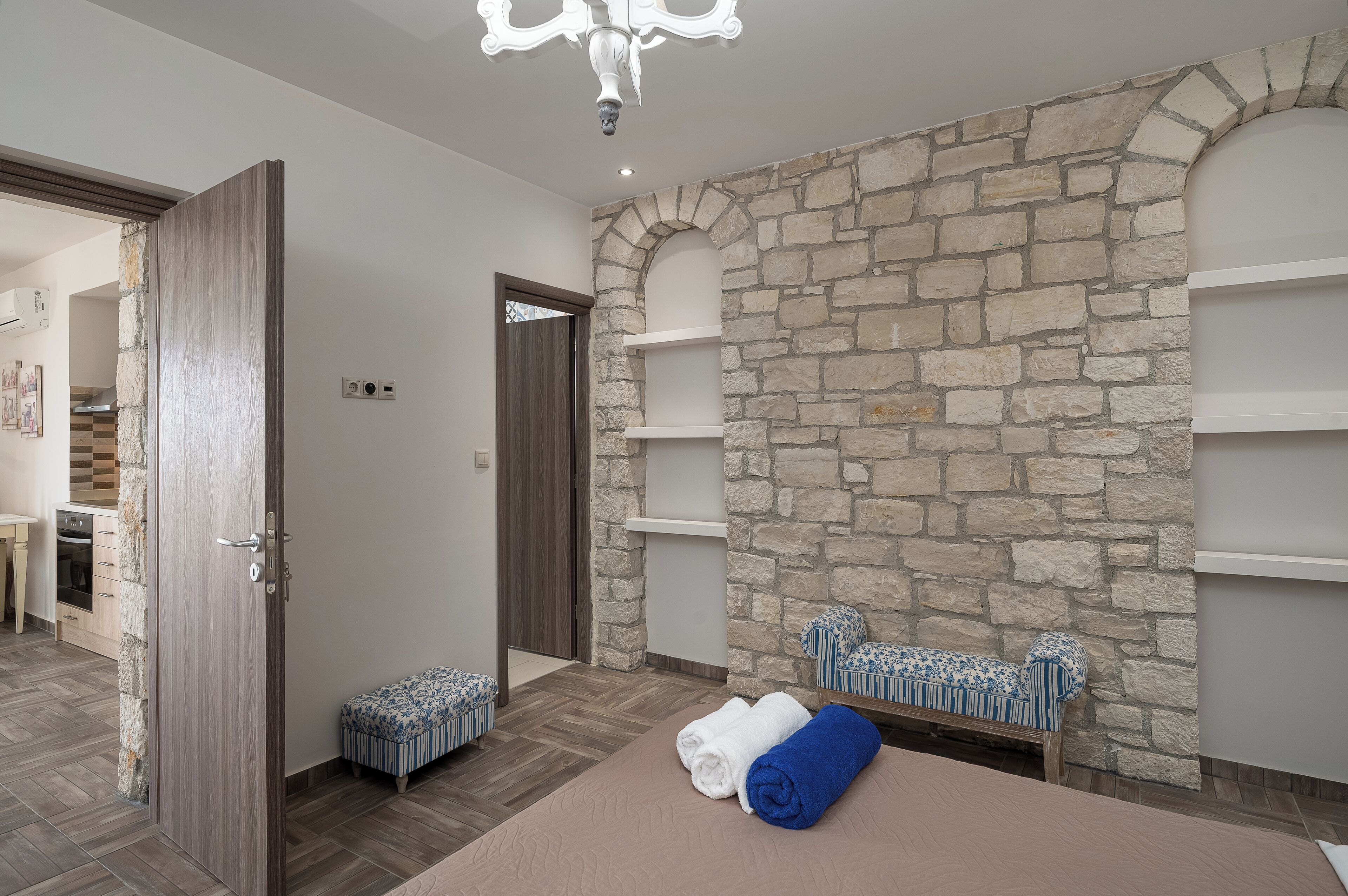 A room with a stone wall, a wooden door, a bench, and a bed with towels.