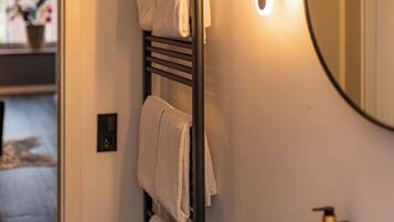 A bathroom with a dark wood towel rack, a white sink, a round mirror, and a wall-mounted light fixture.