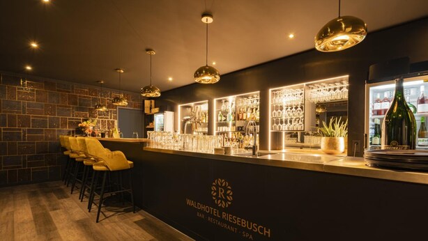 A bar area with a counter, bar stools, and a wine refrigerator. - Waldhotel Riesebusch (Bad Schwartau)