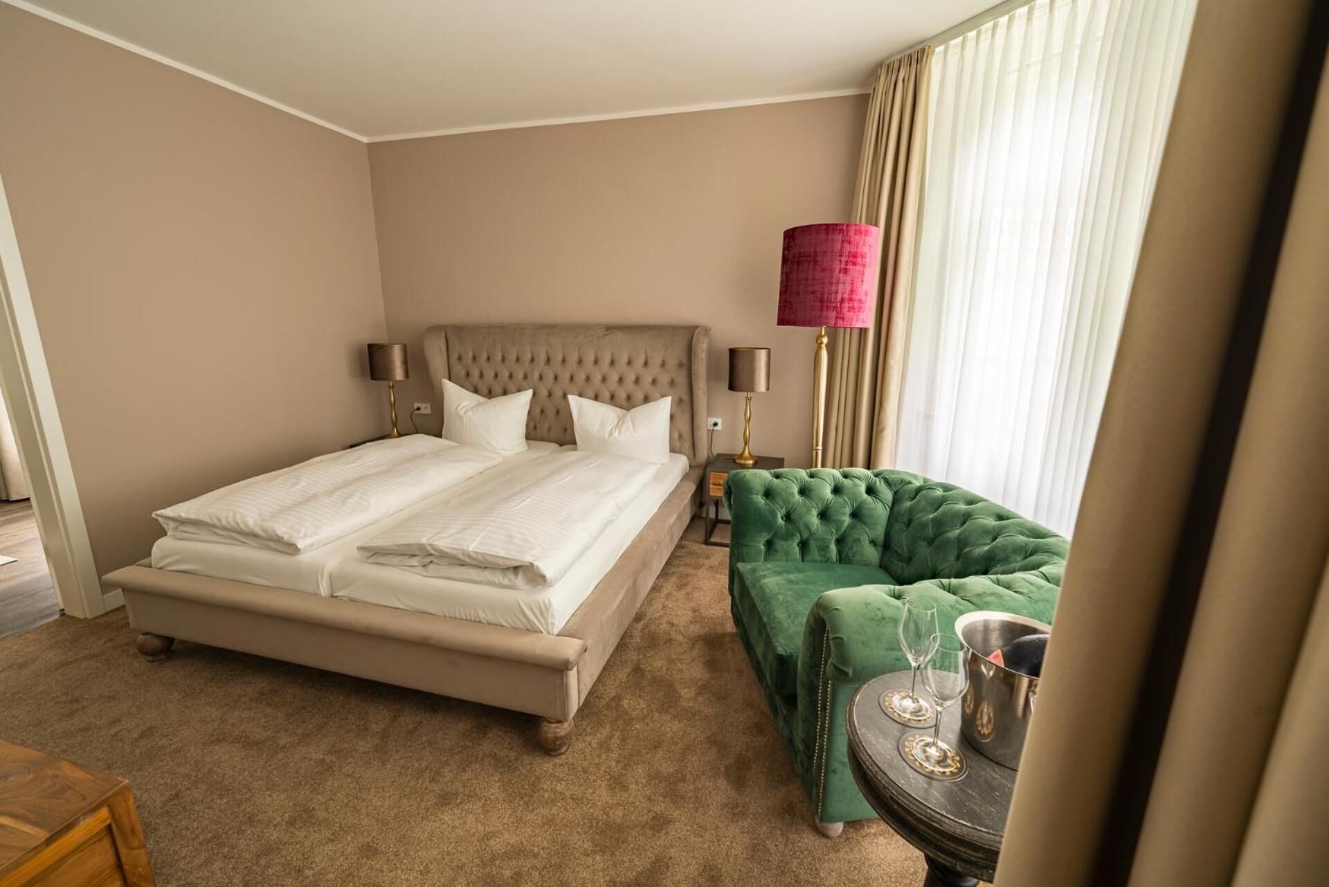 A hotel room with a large bed, a green sofa, a small table with glasses and a bucket, and a lamp.