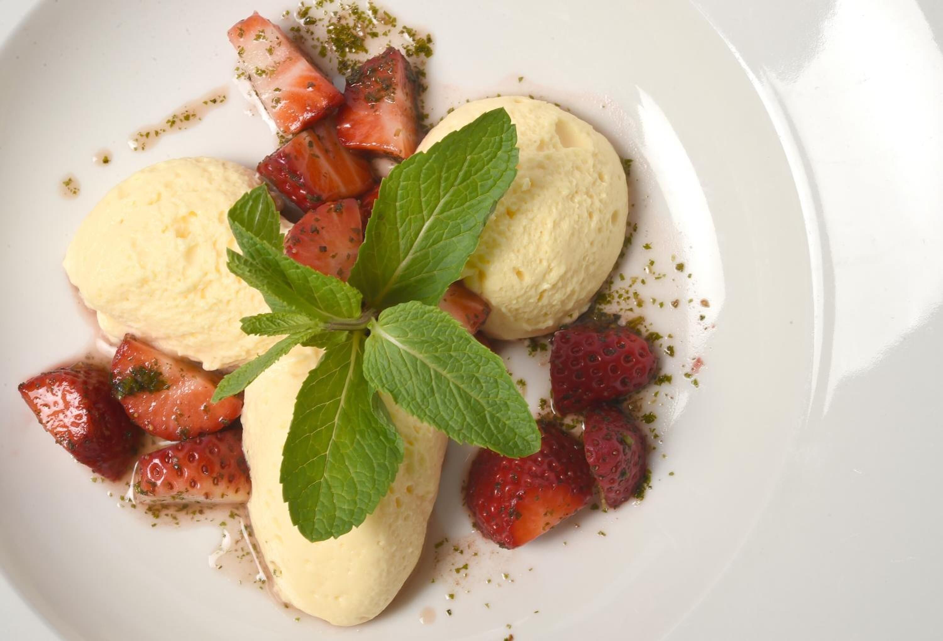 A dessert plate with two scoops of vanilla ice cream, fresh strawberries, and mint leaves.