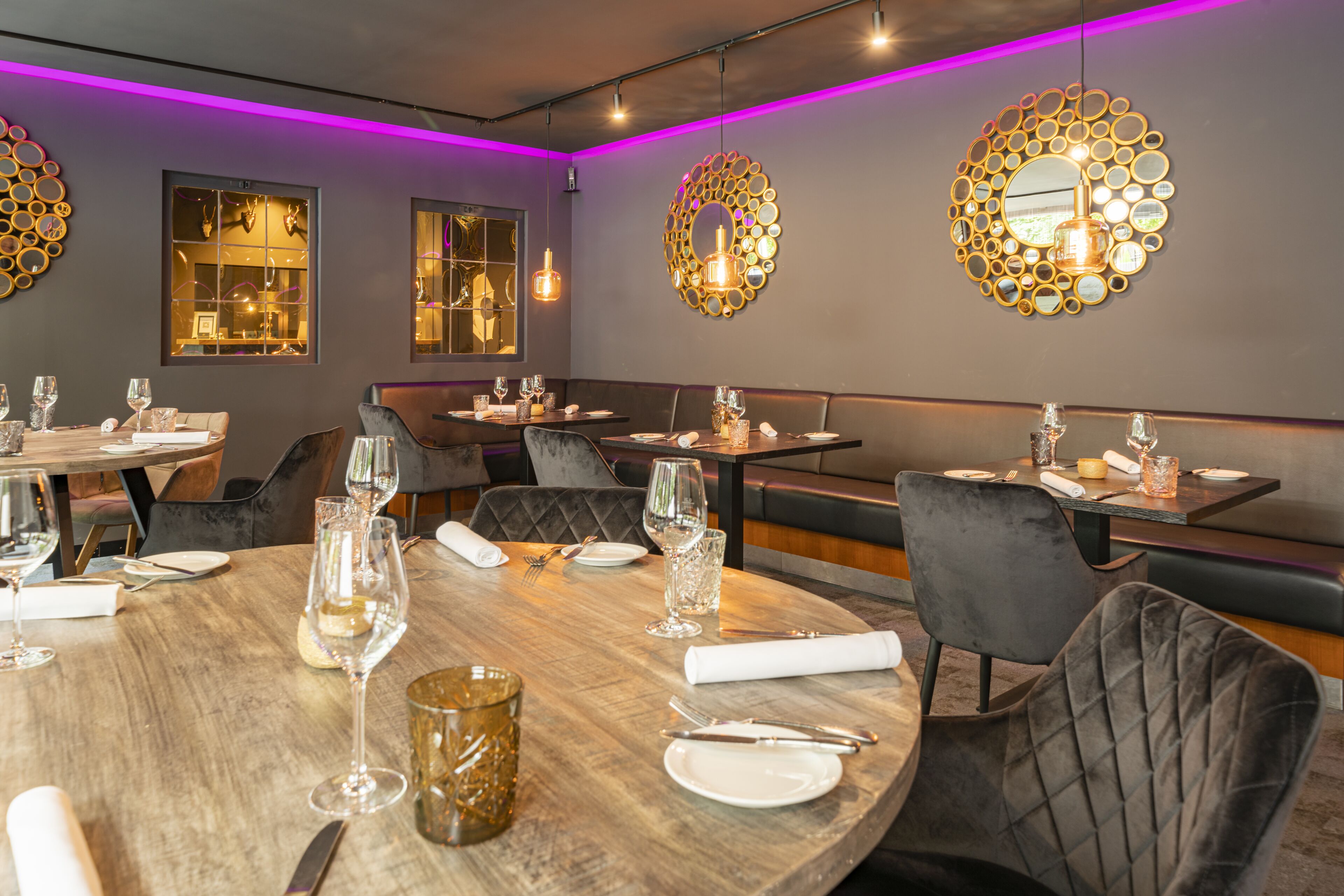 A restaurant with round tables, dark upholstered chairs, and pendant lighting.