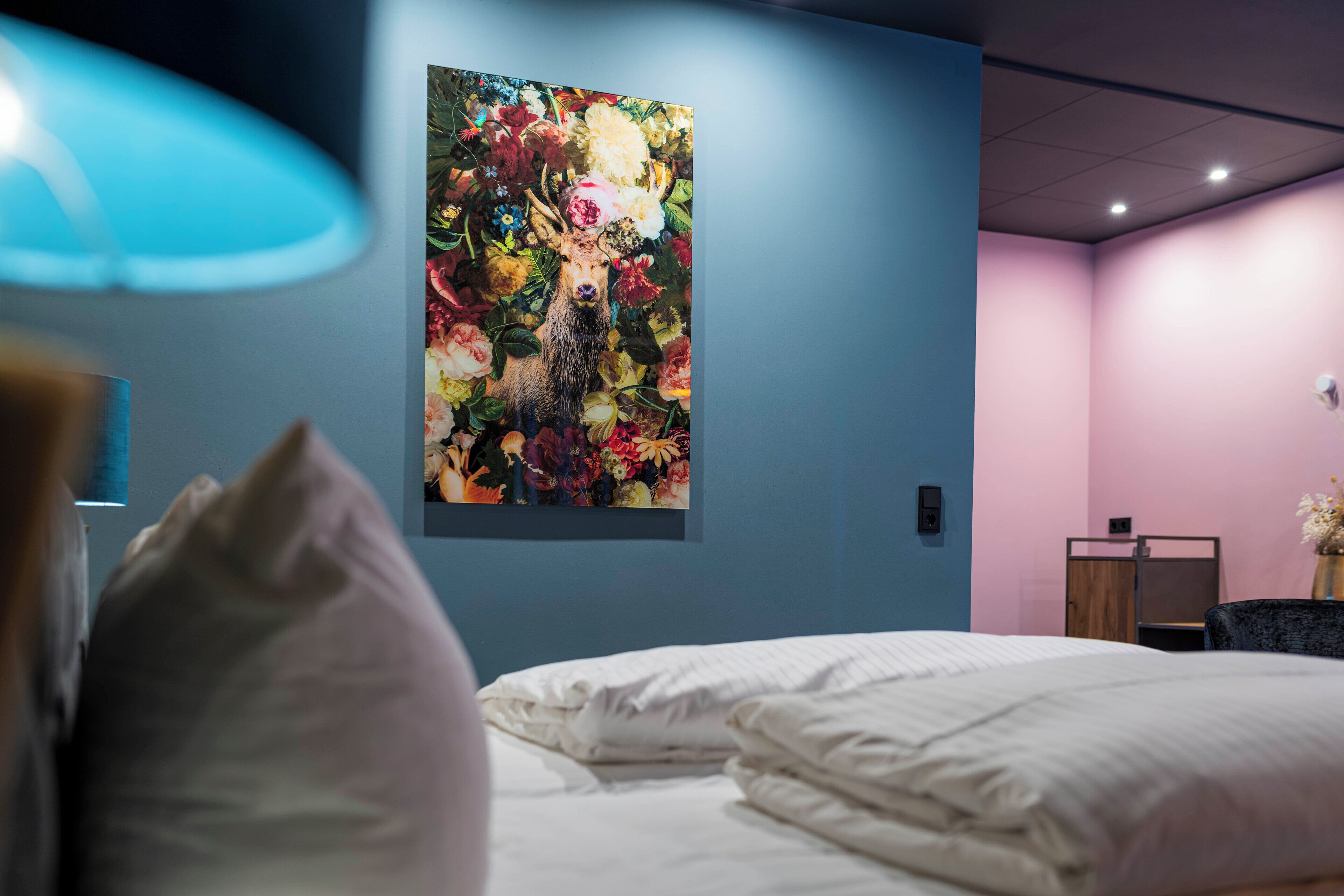 A hotel room with a bed, a wall-mounted painting of flowers, and a desk with a chair.