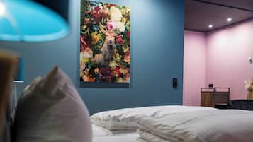 A hotel room with a bed, a wall-mounted painting of flowers, and a desk with a chair.
