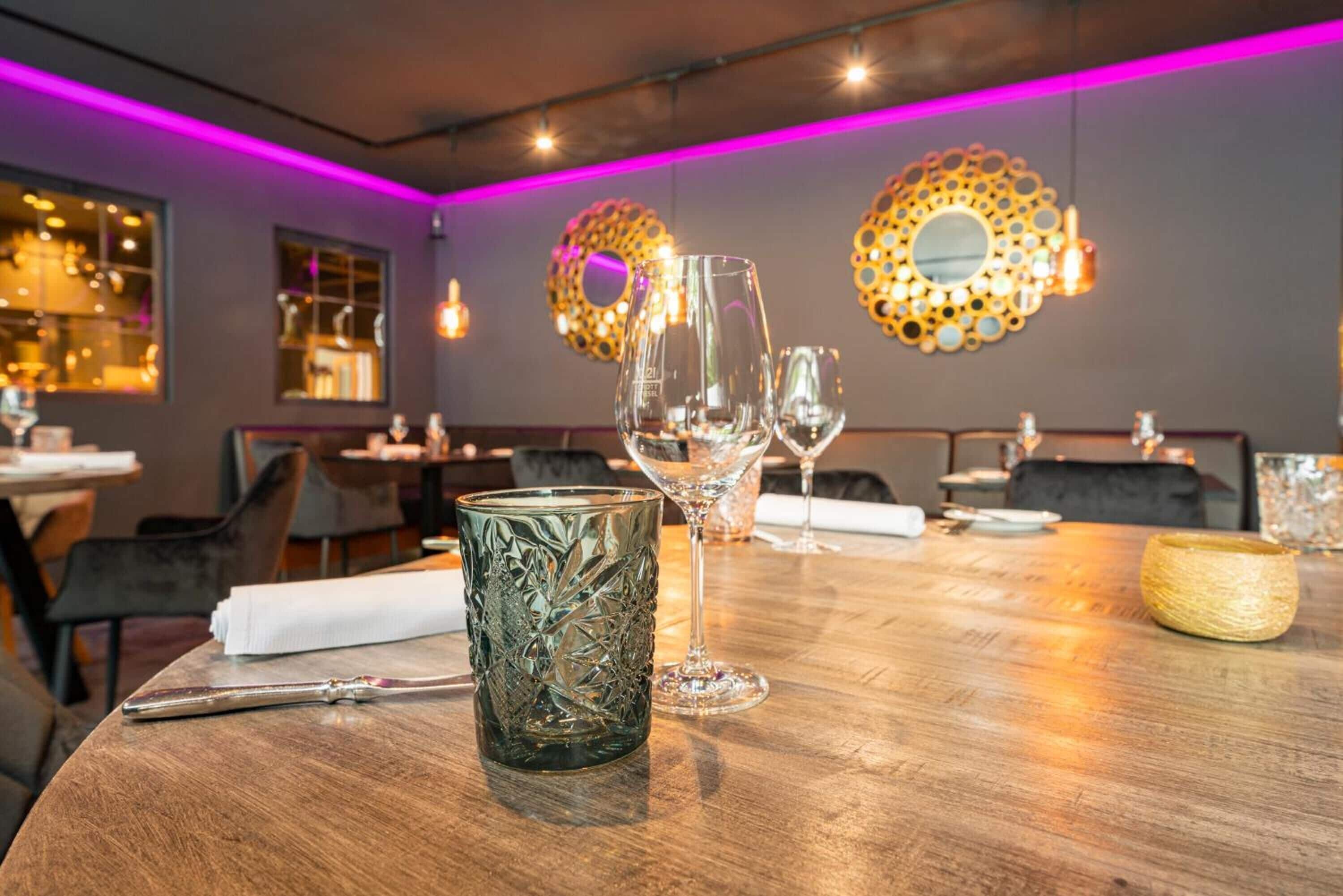 A restaurant interior with a wooden table, clear glassware, and decorative wall mirrors.