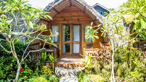 A wooden cabin with a thatched roof, surrounded by lush greenery and a variety of plants. - Cotton Tree Cottages (Gili Trawangan)
