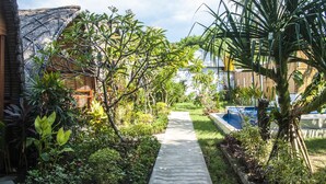A pathway leading through a lush garden with various plants and a pool area. - Cotton Tree Cottages (Gili Trawangan)