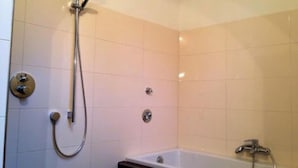 Un baño con una bañera, ducha con cabezal de mano y dos grifos empotrados.
