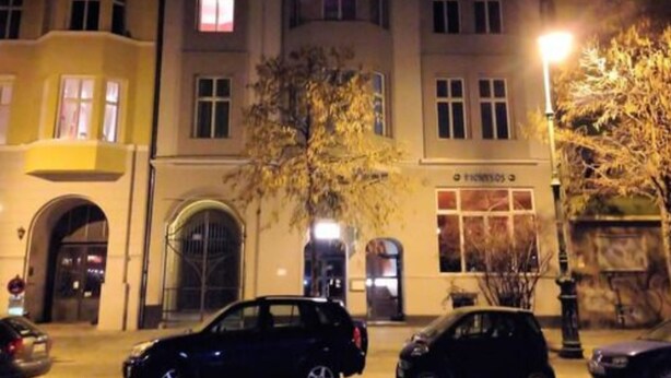Un edificio de varios pisos con una entrada central, ventanas grandes y un árbol en la fachada.