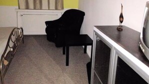 Una habitación con una silla negra, una pequeña mesa con un objeto decorativo y un radiador junto a una pared amarilla.
