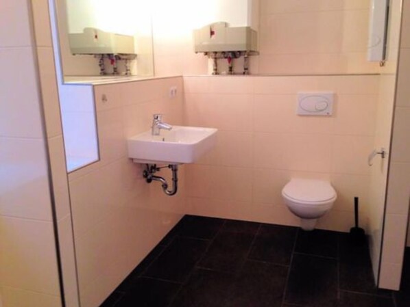 Une petite salle de bain avec un lavabo blanc, des toilettes et un miroir au-dessus du lavabo.