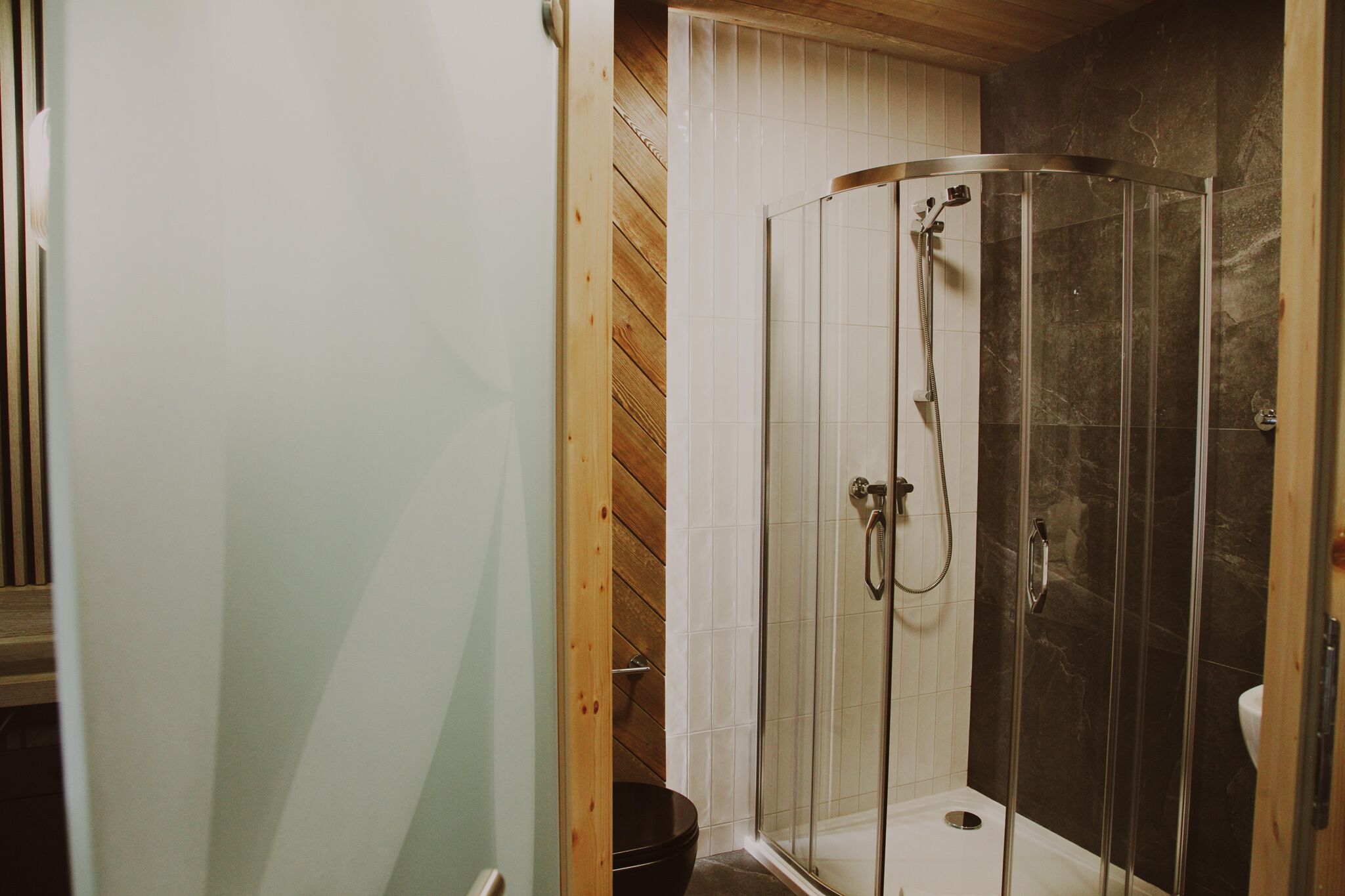 Une douche entièrementClose avec des parois en verre, un intérieur en bois, un mur recouvert de carreaux blancs et un sol en marbre.